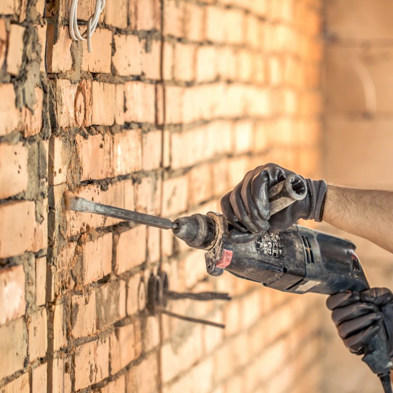 Handyman at a construction site in the process of drilling a wall with a perforator. Copy space.